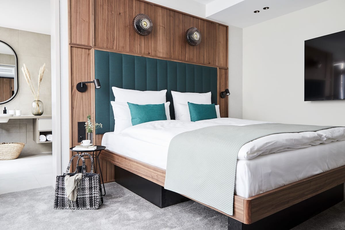Une chambre à coucher moderne avec une tête de lit en bois, du linge de lit blanc et une petite table de chevet avec une lampe.
