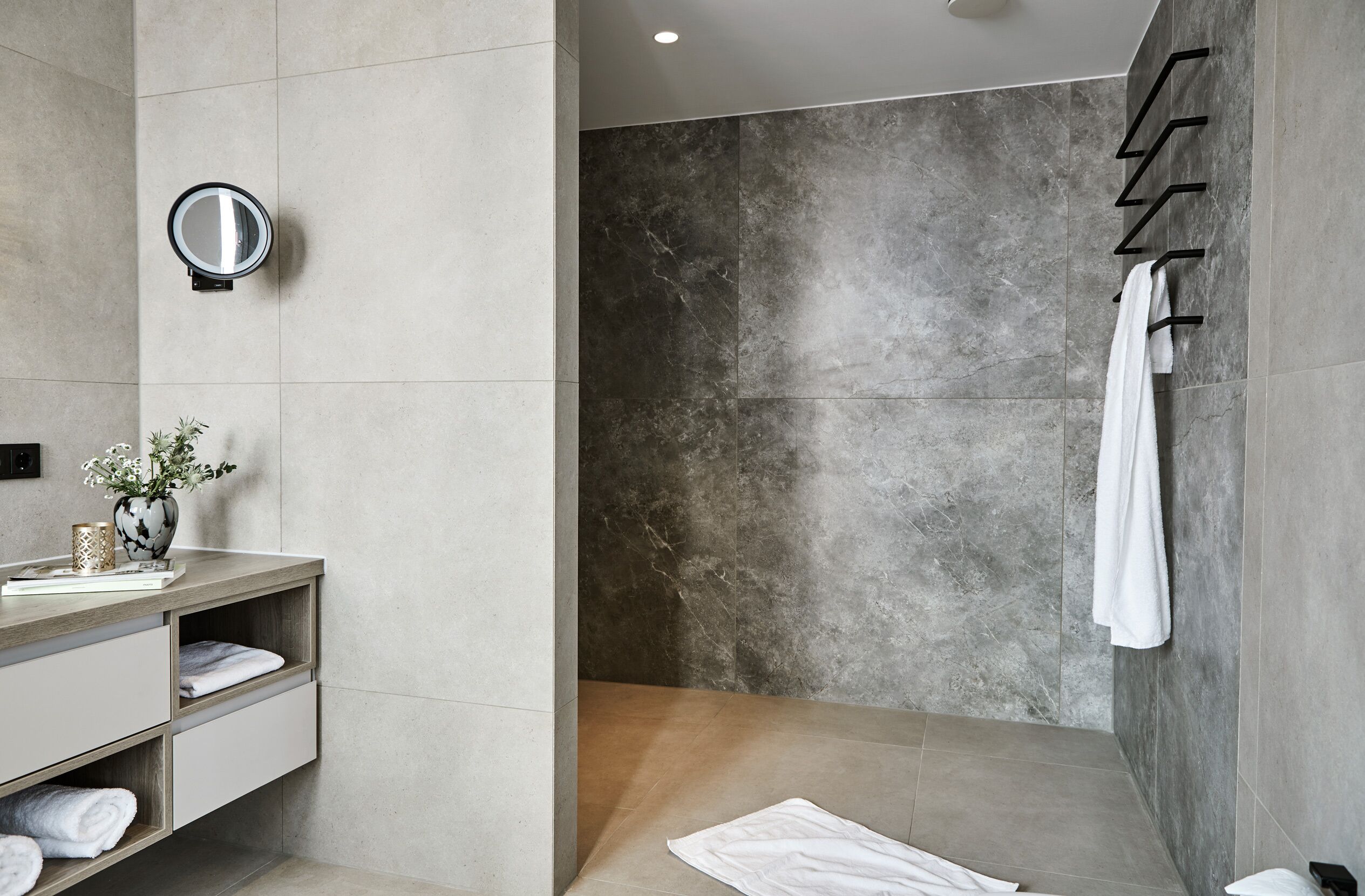 A modern bathroom with a marble shower, a vanity with a mirror, and a towel rack.