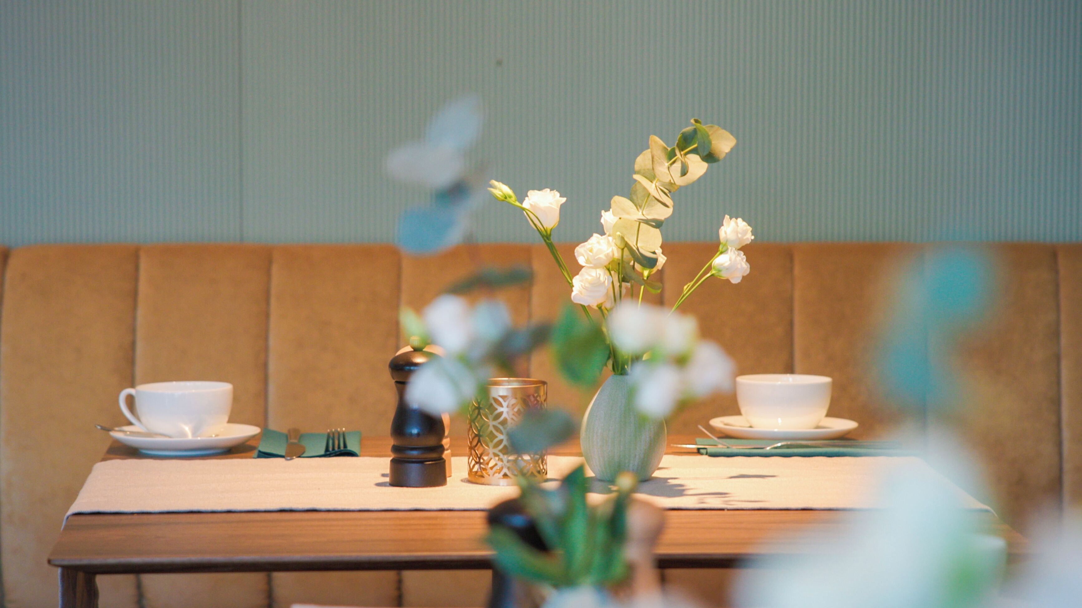 A dining table with white cups and saucers, a vase with white flowers, and a pepper grinder.