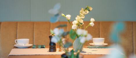 Una mesa de comedor con tazas y platillos blancos, un florero con flores blancas y un molinillo de pimienta.