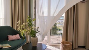 Una sala moderna con un sofá verde, un jarrón blanco con flores y vistas a un balcón.