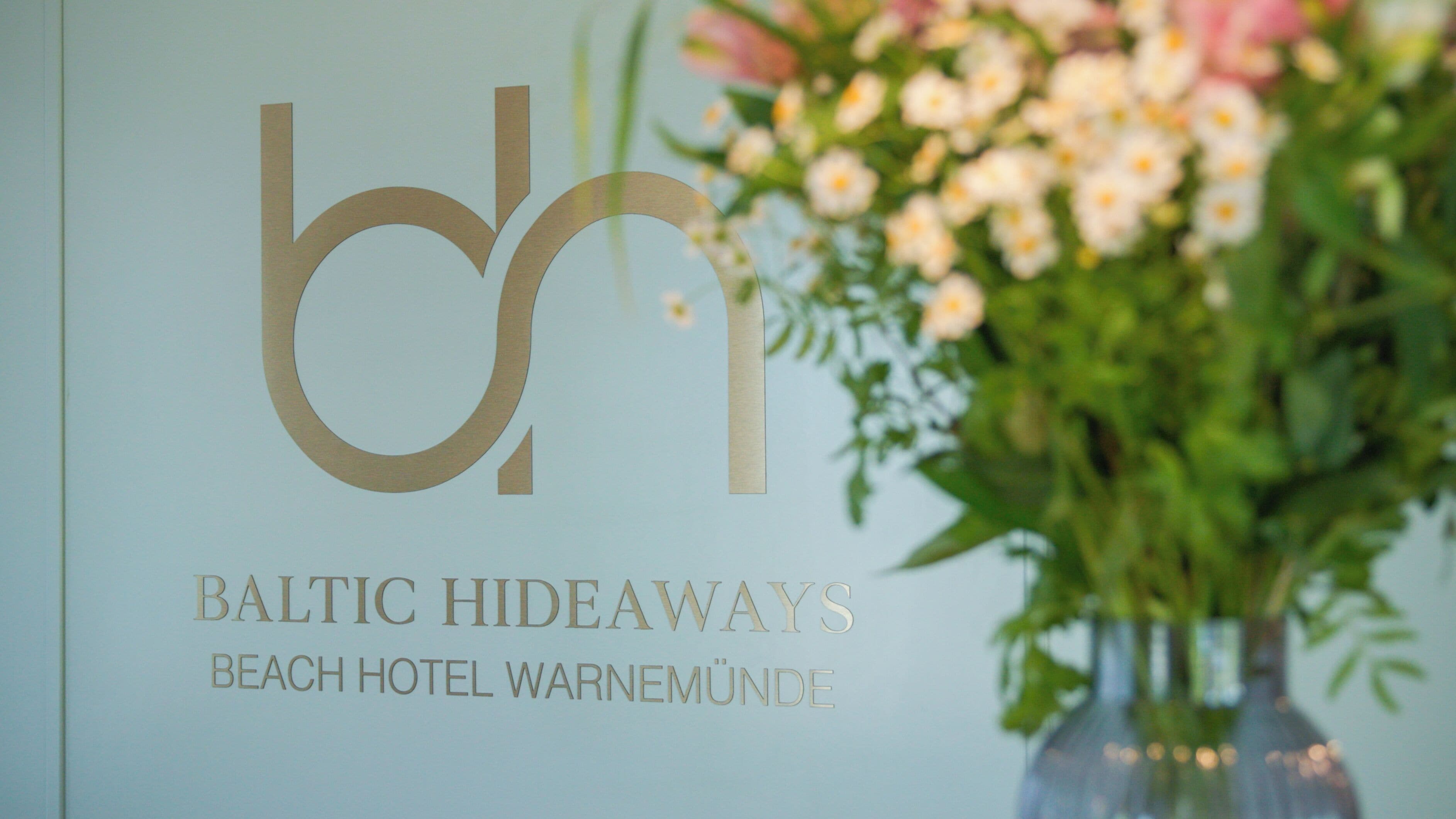 A sign with the logo 'bh' and the text 'Baltic Hideaways Beach Hotel Warnemünde'.