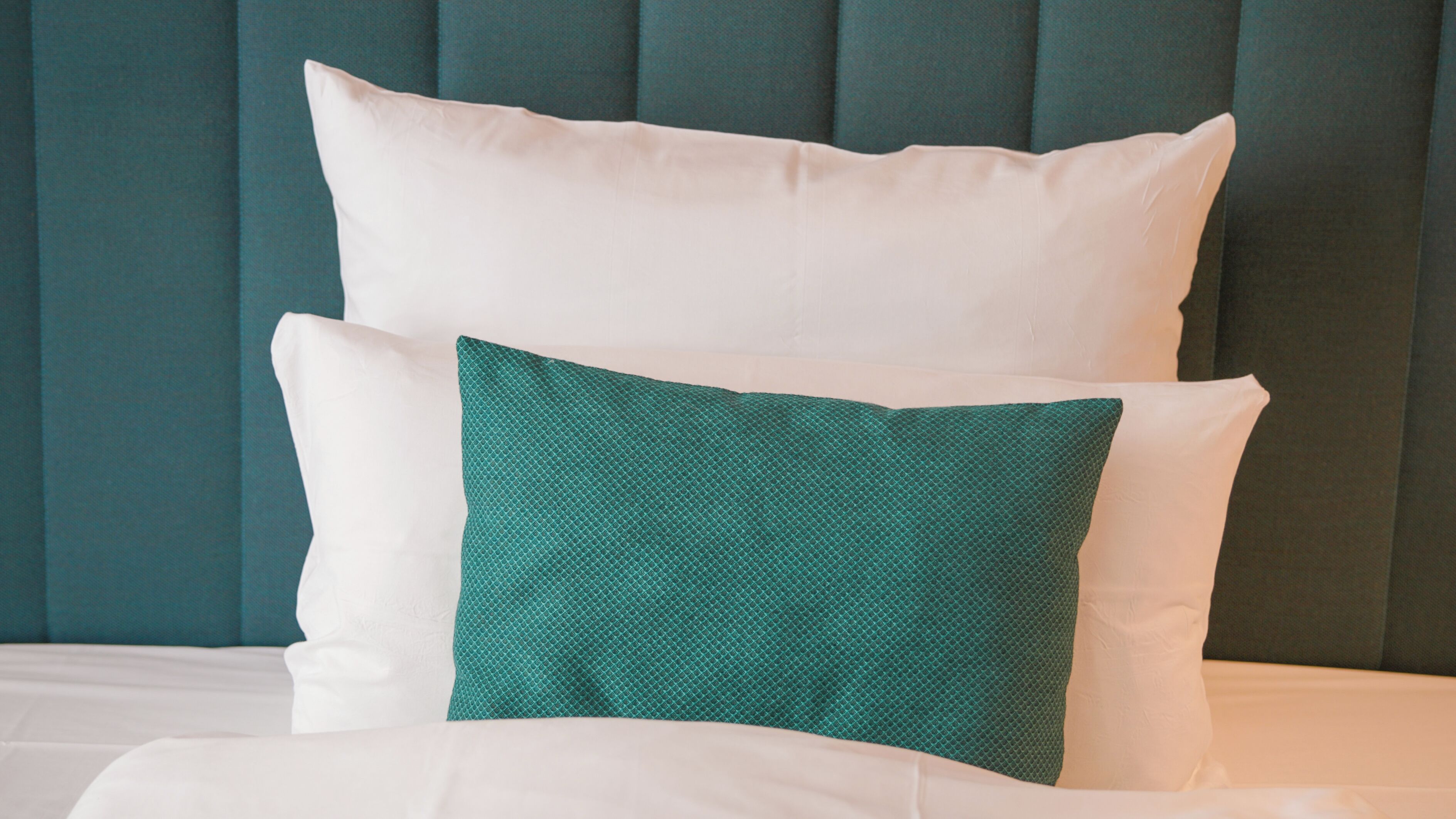 Una cama con almohadas blancas y azul turquesa contra un cabecero azul turquesa.