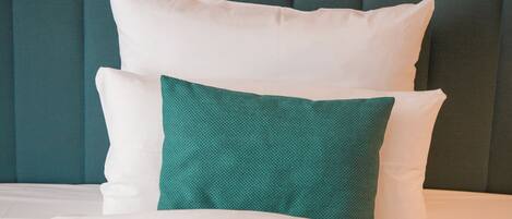 A bed with white and teal pillows against a teal headboard.