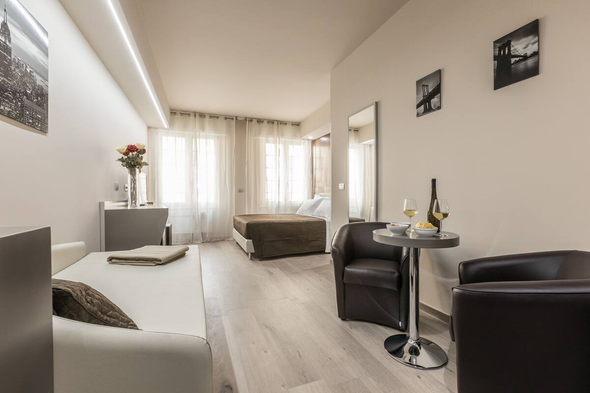 Una habitación de hotel moderna con una cama, una zona de estar con una mesa y un espejo grande.