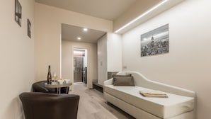Een moderne woonkamer met een bank, een eettafel met een fles en glazen, en een stadsgezichtschilderij aan de muur.