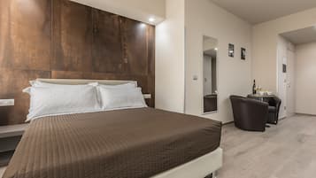 Ein modernes Schlafzimmer mit einem großen Bett, einem hölzernen Kopfteil, einer kleinen Sitzecke mit Stuhl und Tisch sowie einem Spiegel an der Wand.