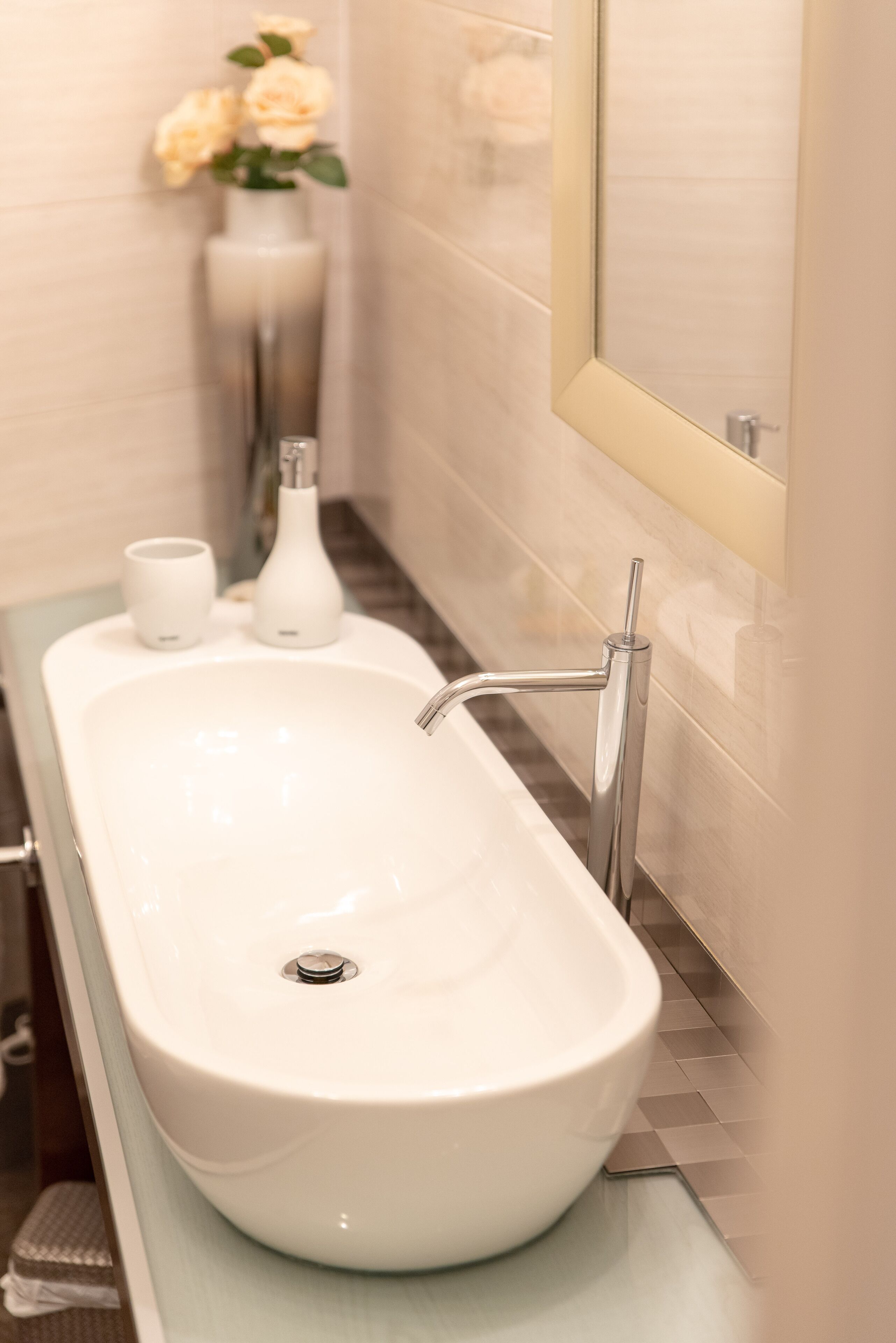 A bathroom with a white sink, a mirror, and a vase with flowers.