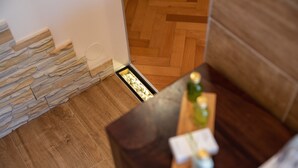A corner of a room with a wooden floor, a stone wall, and a dark wooden table with a bottle and a card on it.