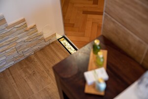 Un rincón de una habitación con suelo de madera, pared de piedra y una mesa de madera oscura con una botella y una tarjeta encima.