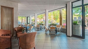 An indoor patio area with tiled flooring, wicker chairs, and tables. - Hotel Foglieri (Cesenatico)