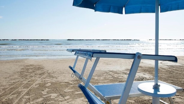 A beach chair with a blue umbrella, a sandy beach, and a calm sea in the background. - Hotel Foglieri (Cesenatico)