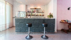 A bar area with two stools, a stone countertop, and a variety of bottles and glasses. - Hotel Foglieri (Cesenatico)
