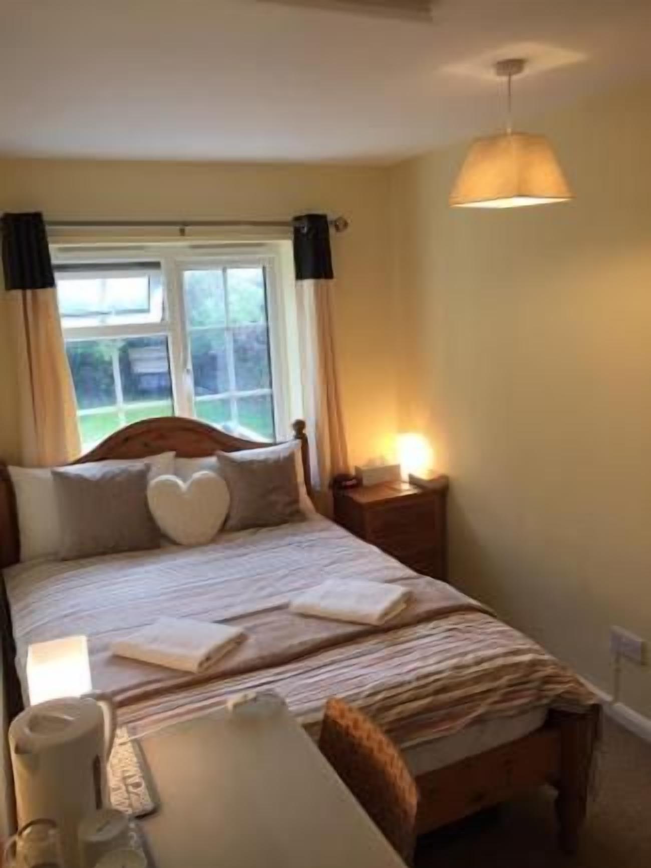 A bedroom with a bed, bedside table, lamp, and window with curtains.