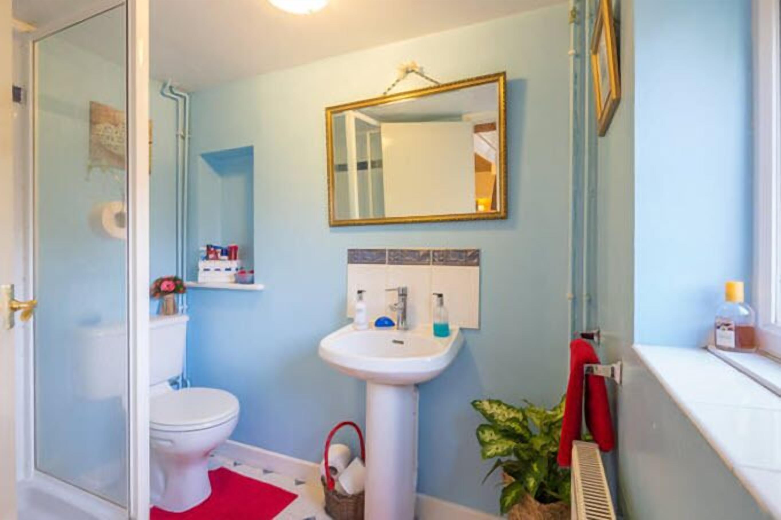 A bathroom with a white toilet, a pedestal sink, a mirror, and a window with a towel hanging on the sill.