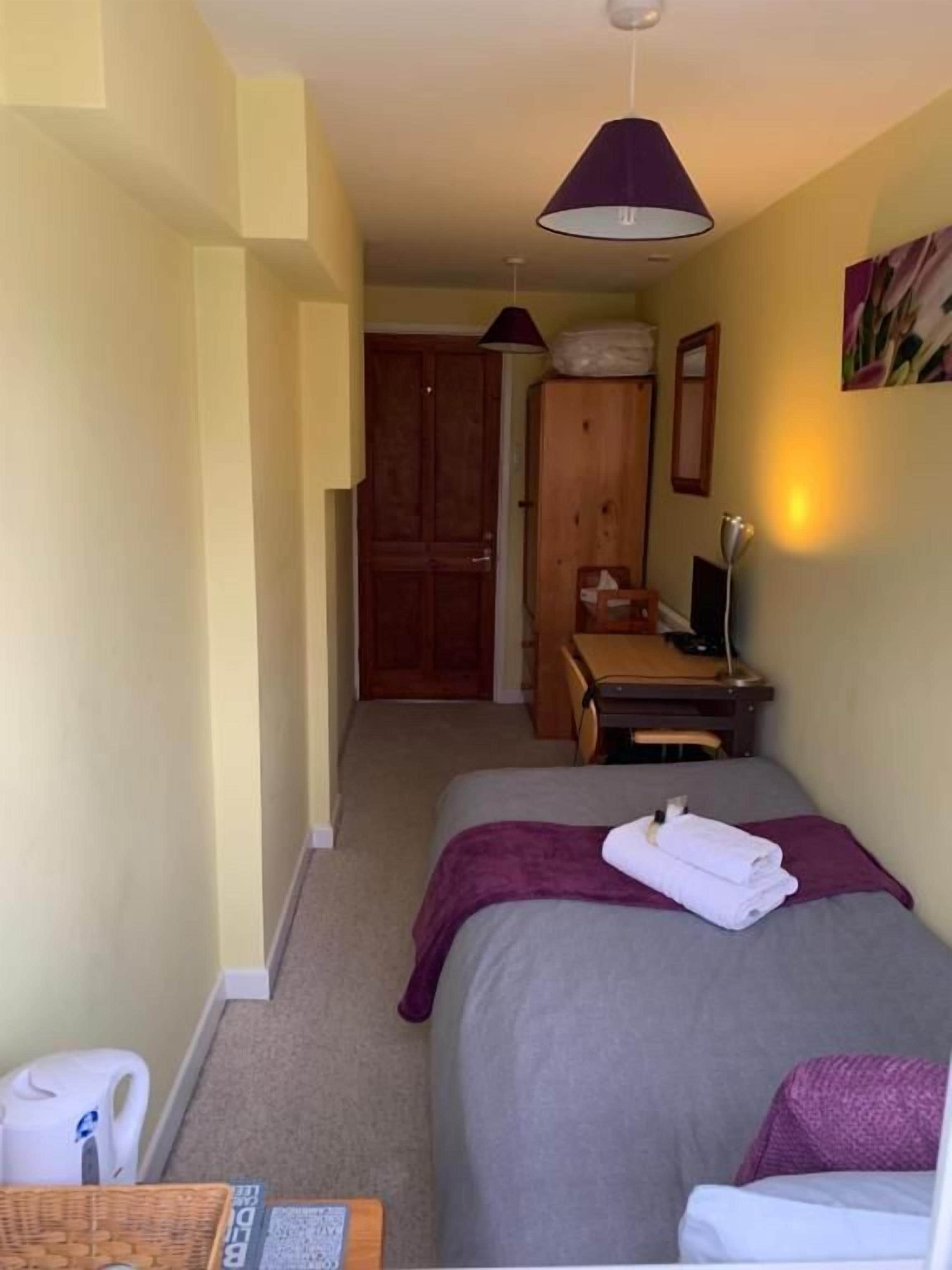 Una habitación de hotel con una cama, un escritorio, una silla, un armario y una puerta que da a otra habitación.