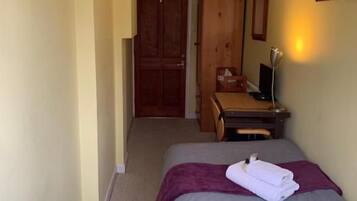 Una habitación de hotel con una cama, un escritorio, una silla, un armario y una puerta que da a otra habitación.