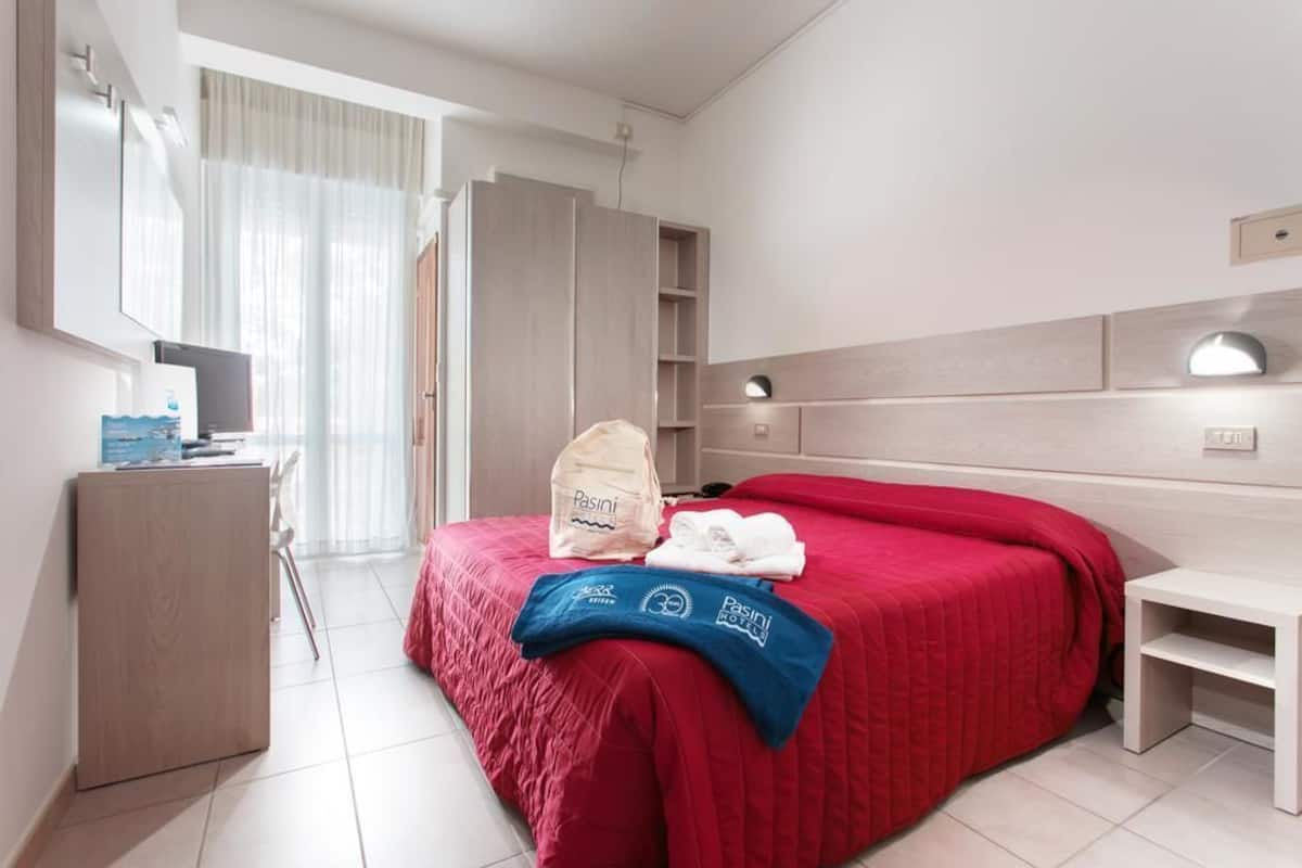 A hotel room with a bed, a desk, a wardrobe, and a mirror.