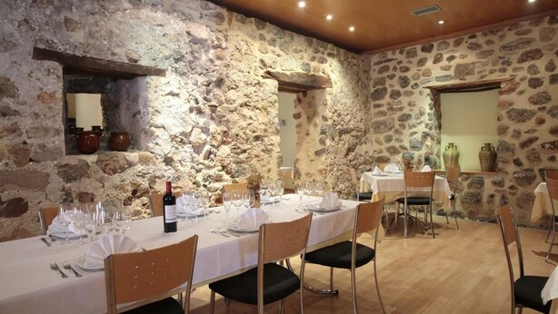 A dining area with a stone wall, wooden ceiling, and a table set for four with chairs. - Hotel Casa Palacio (Montanejos)