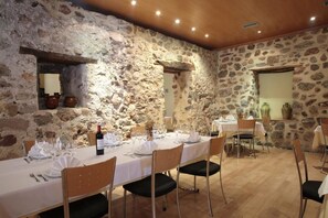 A dining area with a stone wall, wooden ceiling, and a table set for four with chairs. - Hotel Casa Palacio (Montanejos)