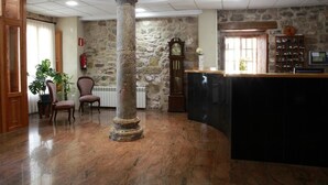 A lobby with a stone column, a reception desk, and a clock. - Hotel Casa Palacio (Montanejos)