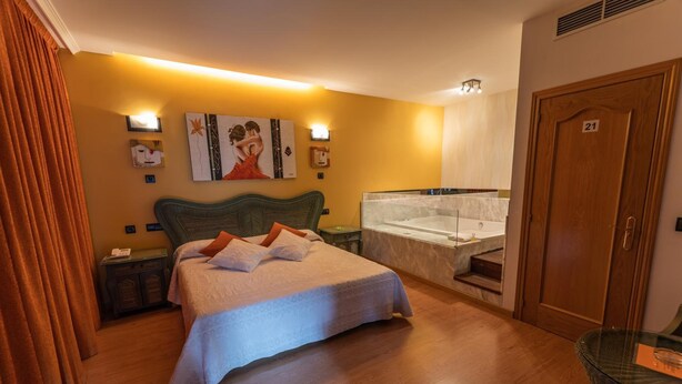 Una habitación de hotel con una cama grande, una bañera, una puerta de madera y una pequeña mesa.