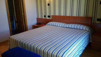 Una habitación de hotel con una cama grande, cabecero de madera, mesita de noche con un teléfono y una lámpara fijada a la pared.