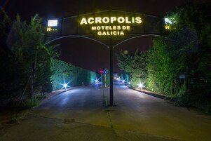 Señalización de 'Acropolis Moteis de Galicia' con una carretera despejada que lleva a la entrada, rodeada de vegetación.