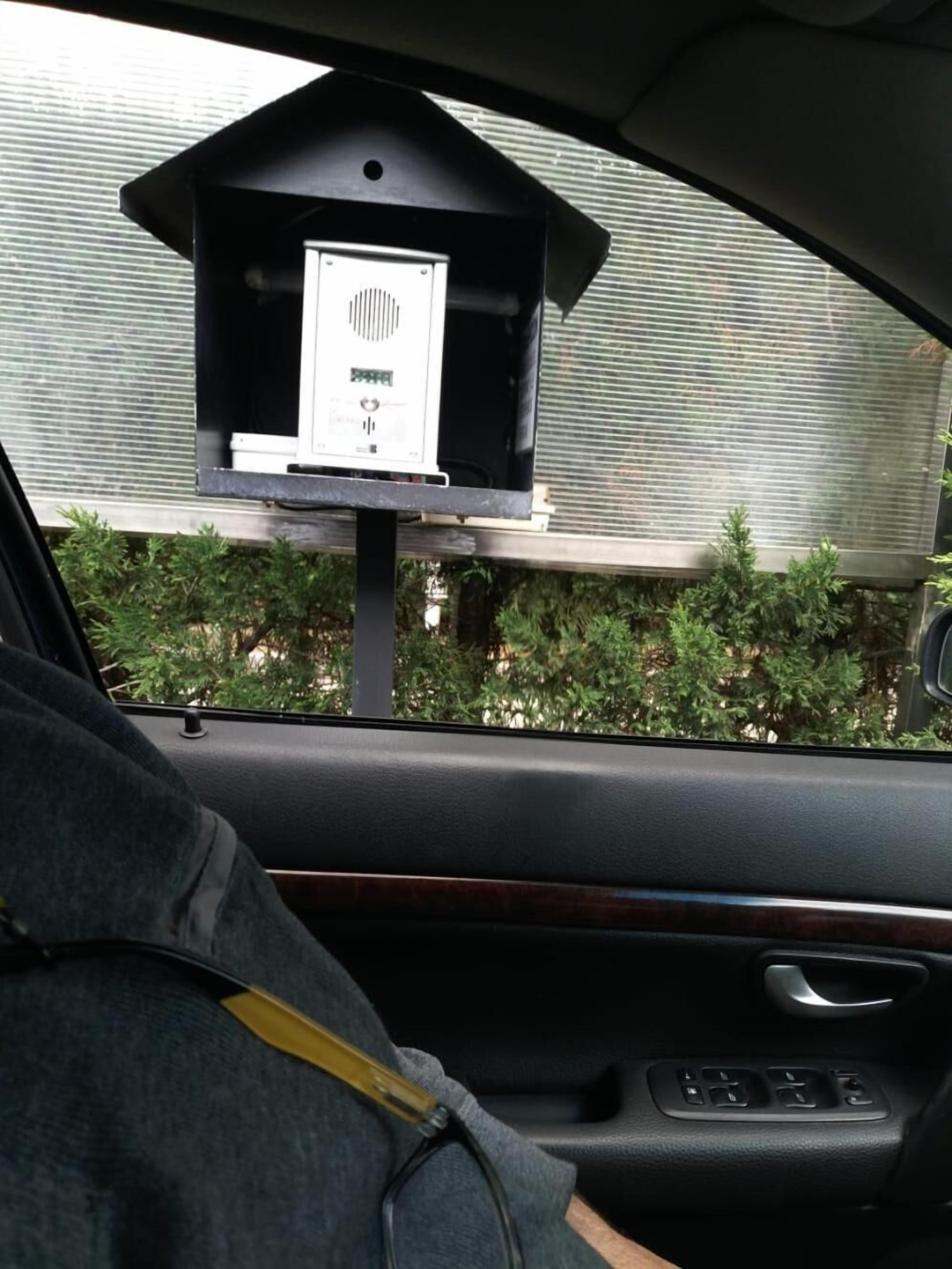 Interior de un coche con un dispositivo montado en el tablero, una ventana con persianas y vistas a la vegetación exterior.