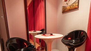Una habitación con tres taburetes negros, una mesa redonda blanca y un espejo que refleja una cortina roja.