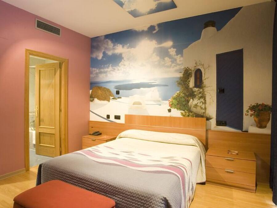 Ein Schlafzimmer mit Wandgemälde einer Küstenlandschaft, einer Holztür, einem Bett mit gemustertem Überwurf und einem Nachttisch.