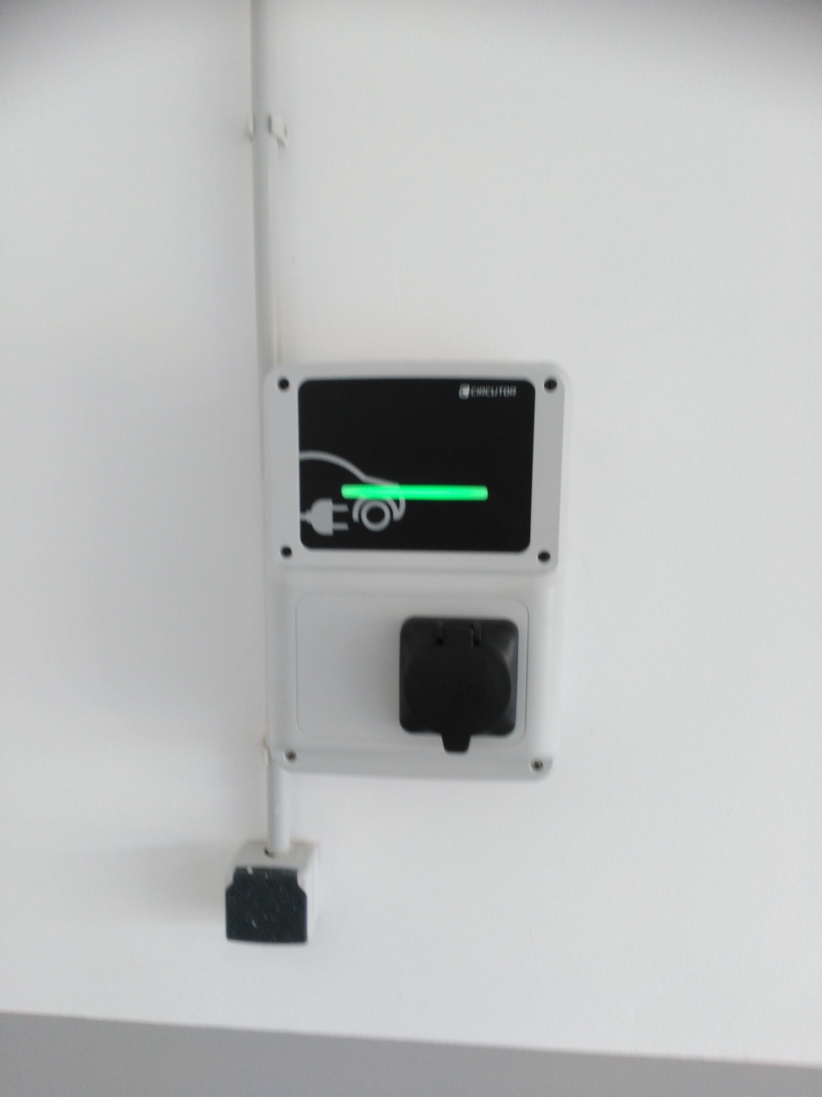 Toma de corriente fijada a la pared, con símbolo de enchufe y luz indicadora verde.