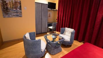 Una habitación con cortina roja, dos sillas de mimbre, una mesita y un televisor sobre un mueble.