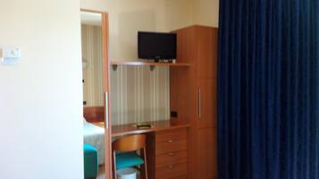 Een slaapkamer met een bed, een bureau, een stoel, een televisie op een plank en een kledingkast.