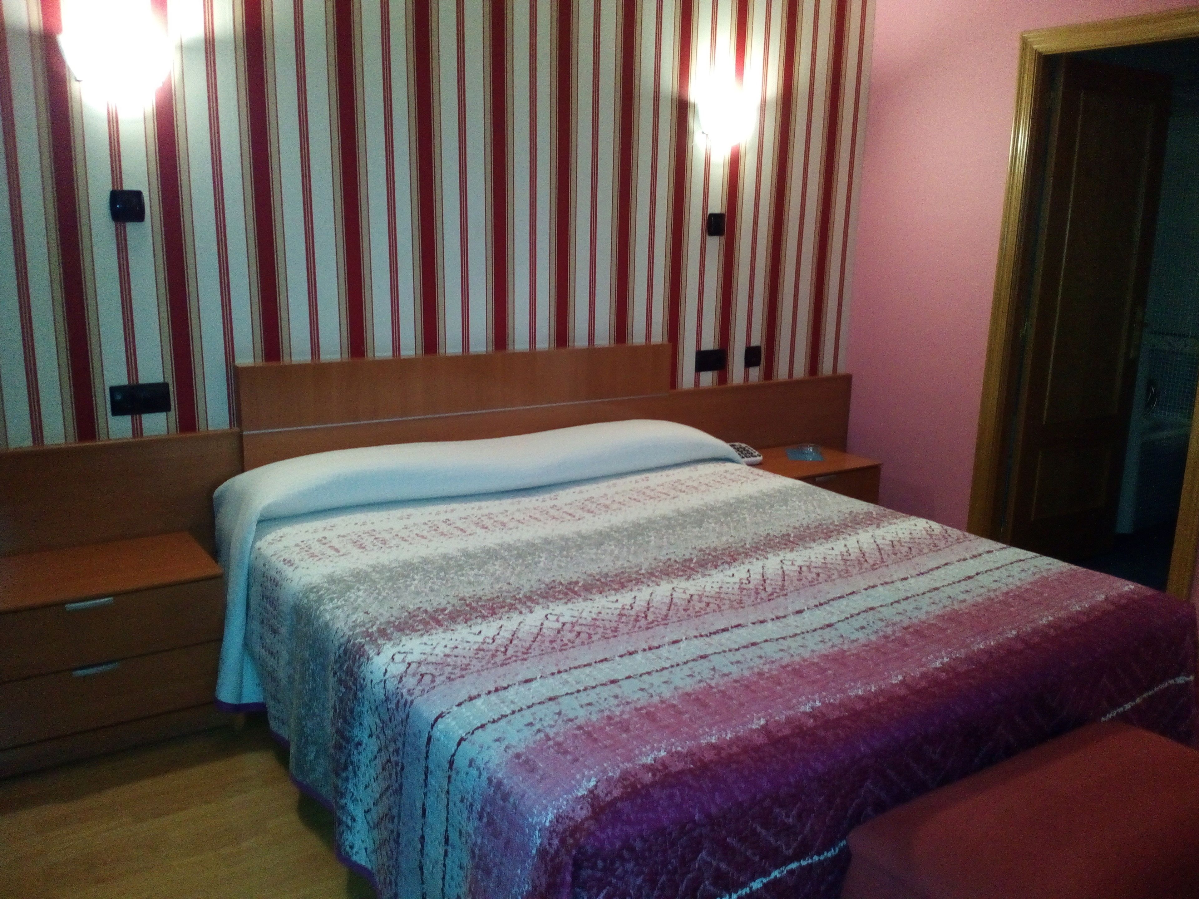 A bedroom with a bed, wooden headboard, bedside tables, and a striped wall.
