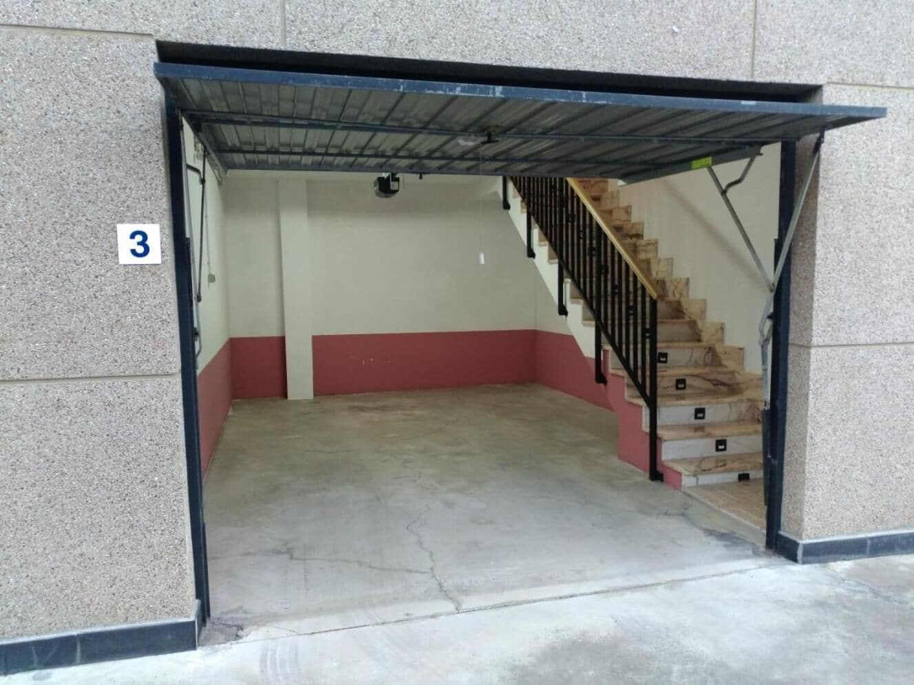A stairwell with a red and white wall, a concrete floor, and a metal railing.