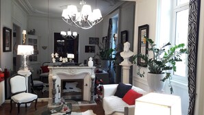 A well-lit living room with a fireplace, a chandelier, and various decorative items. - Les Lamartine (Le Mans)