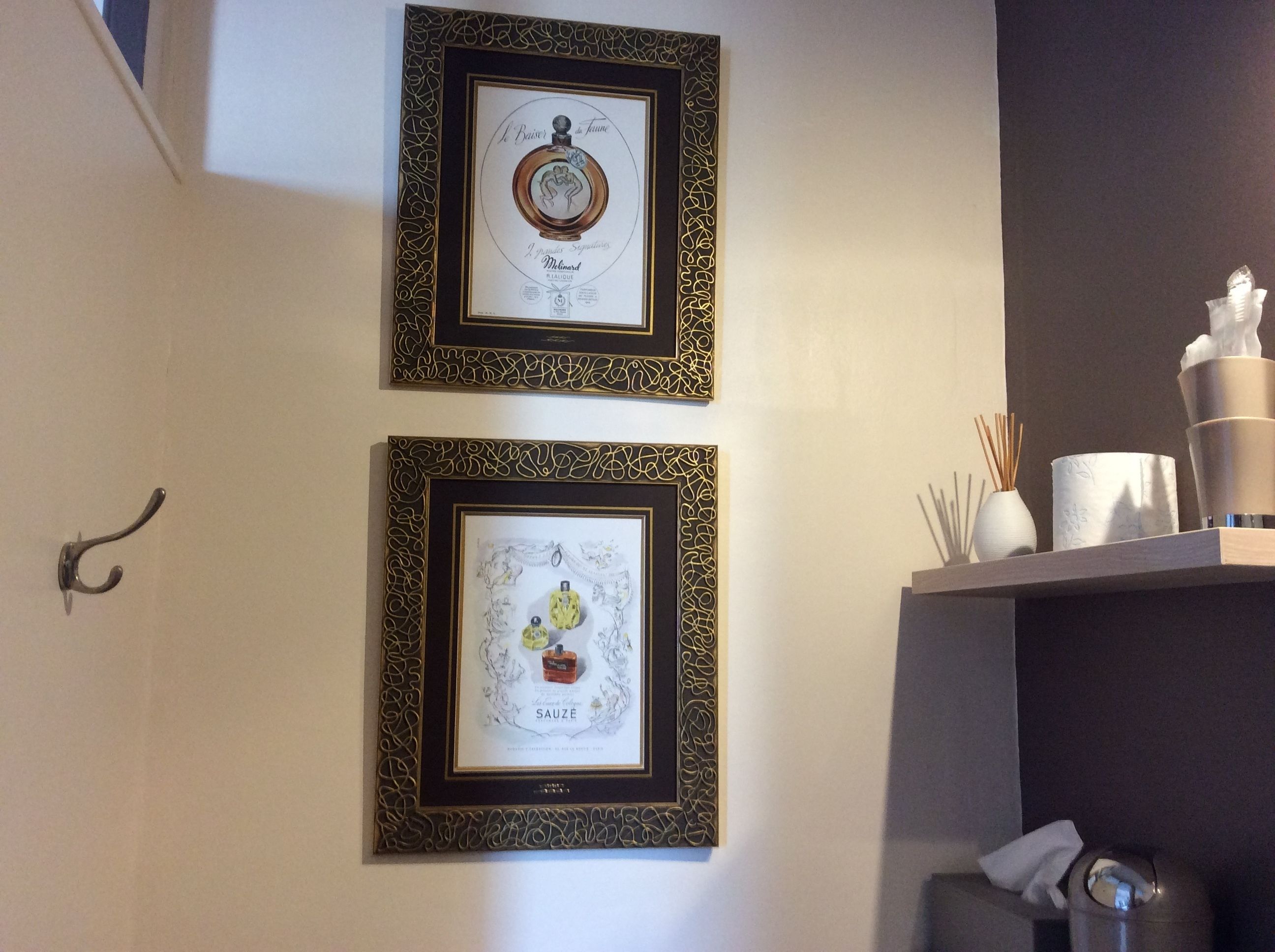 Two framed artworks on a wall, a hook on the left, and a shelf with items on the right.