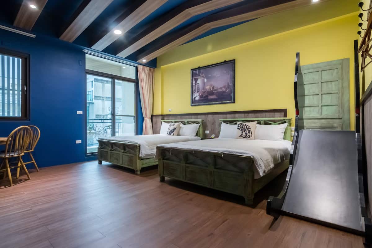 A room with two wooden beds, a dining table with chairs, and a large window with curtains.
