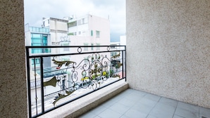 Een balkon met een decoratieve metalen balustrade, een betegelde vloer en een uitzicht op gebouwen in de verte.