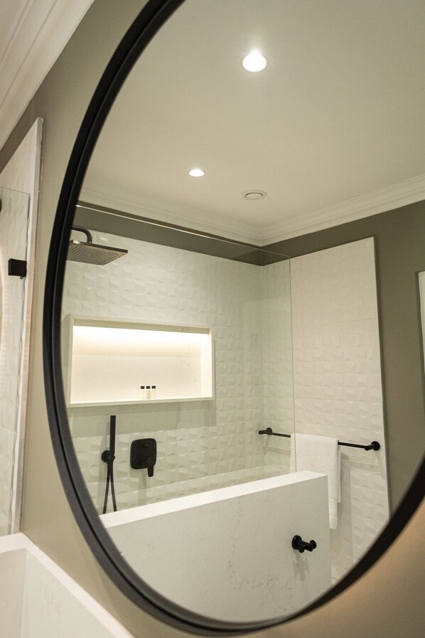 A bathroom with a white tiled wall, a large mirror, a shower, and a towel rack. - Cape Village Lodge (Cape Town)