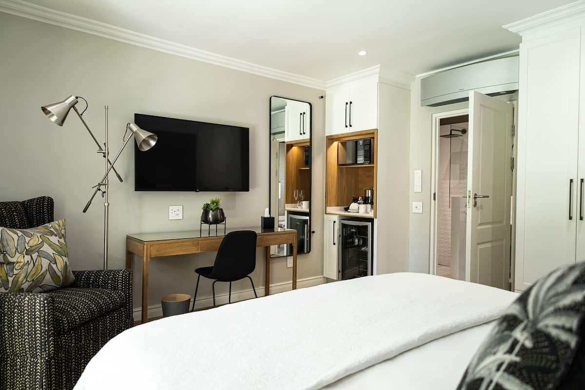 A hotel room with a bed, a desk with a chair, a television, a wardrobe, and a small kitchenette.