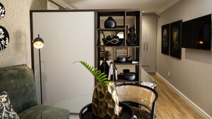 A modern living room with a green sofa, a glass coffee table, and a decorative vase. A bookshelf filled with various items is visible in the background. - Cape Village Lodge (Cape Town)