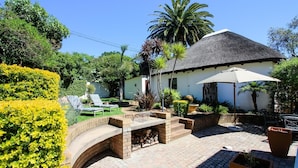 A patio area with a brick fire pit, lounge chairs, and a thatched-roof building. - Cape Village Lodge (Cape Town)