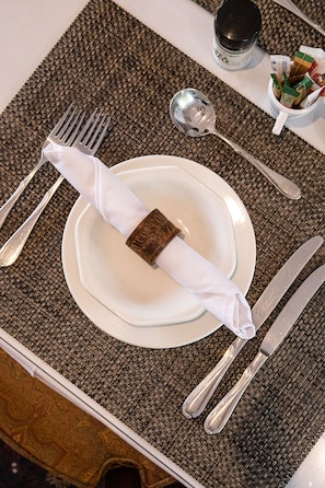 A neatly set dining table with a white plate, a folded napkin, and silver cutlery. - Cape Village Lodge (Cape Town)