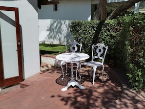 A patio with a white metal table and chairs, a brick pathway, and a white wall. - Cape Village Lodge (Cape Town)