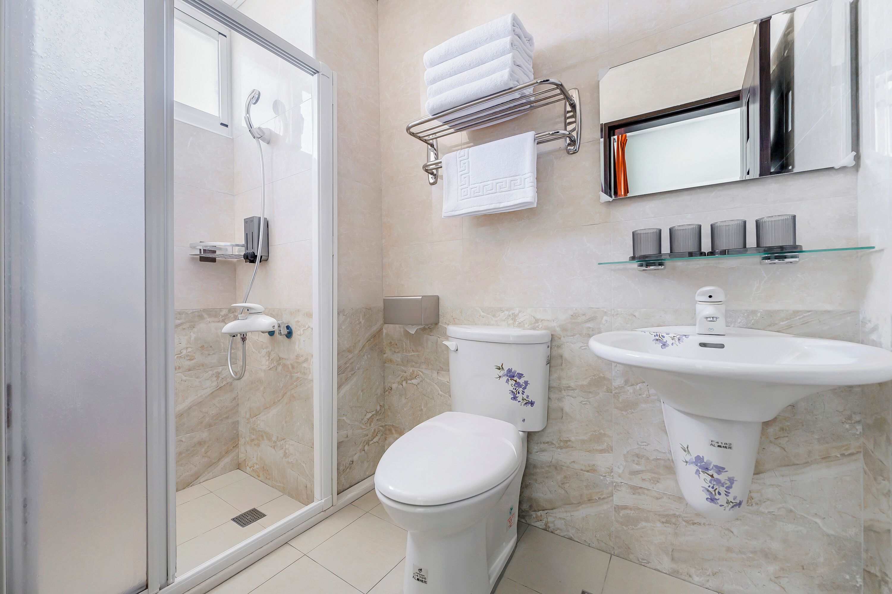 Un baño con cabina de ducha de vidrio, inodoro, lavabo con espejo y toallero con toallas dobladas.