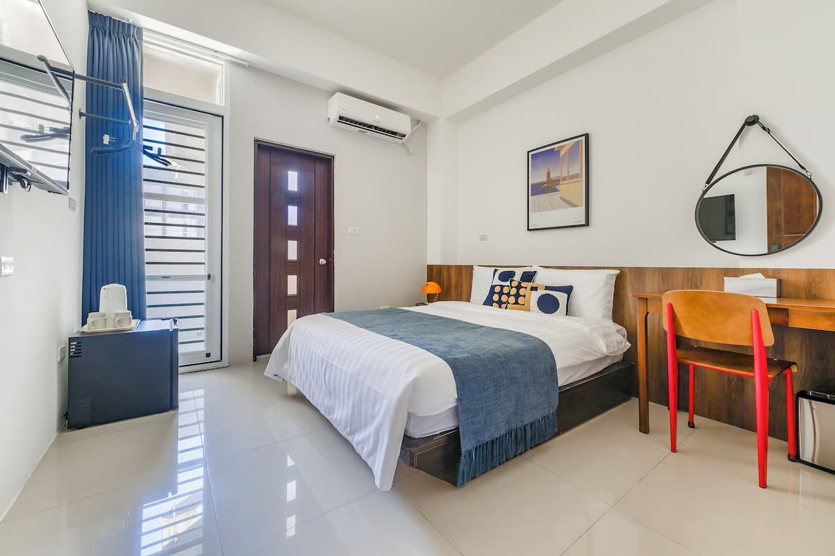Une chambre d’hôtel moderne équipée d’un lit, d’un bureau, d’une chaise, d’une armoire et d’une salle de bain.