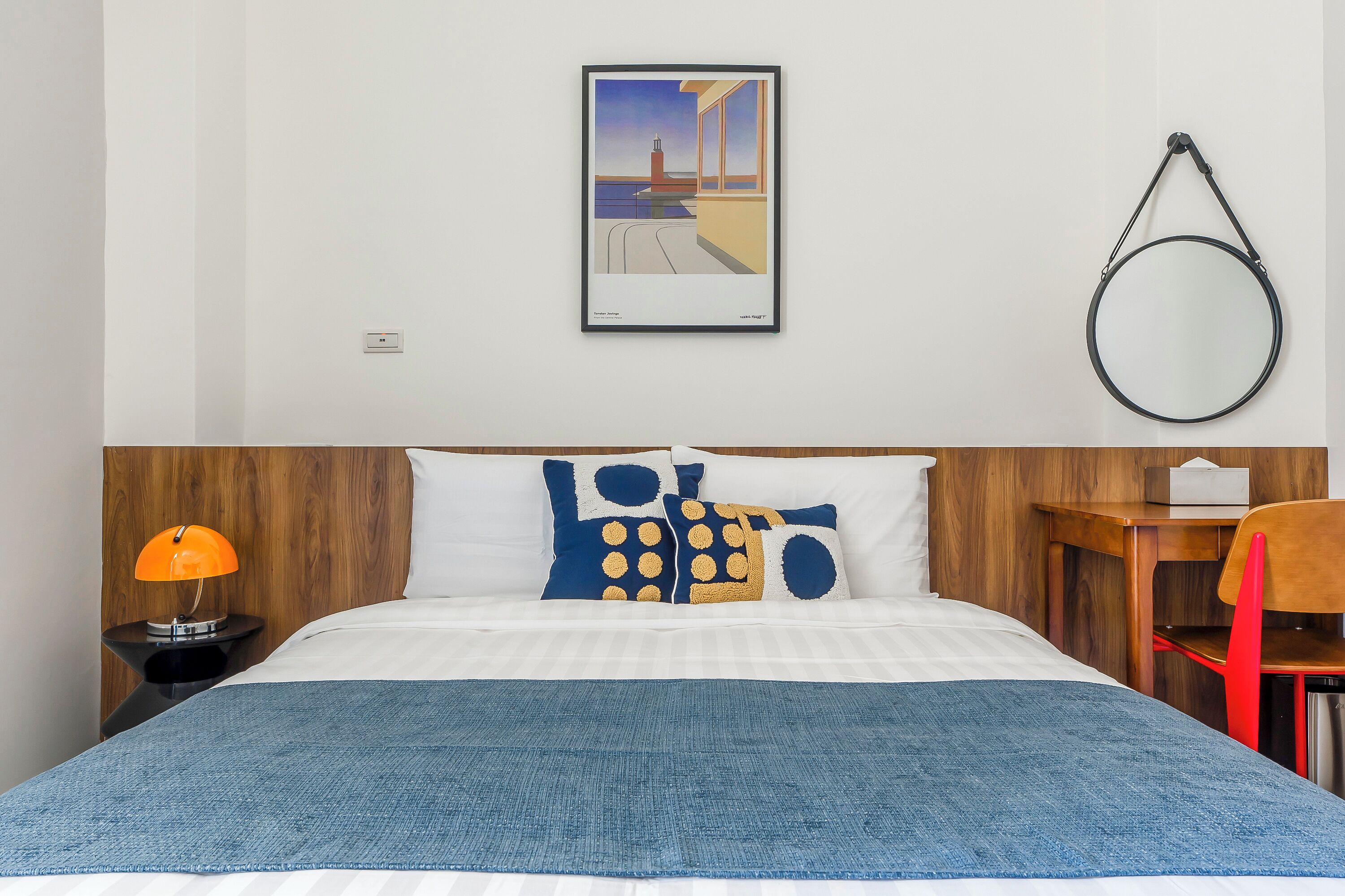 Un letto rifatto con una coperta blu, una testiera in legno e un quadro appeso al muro.