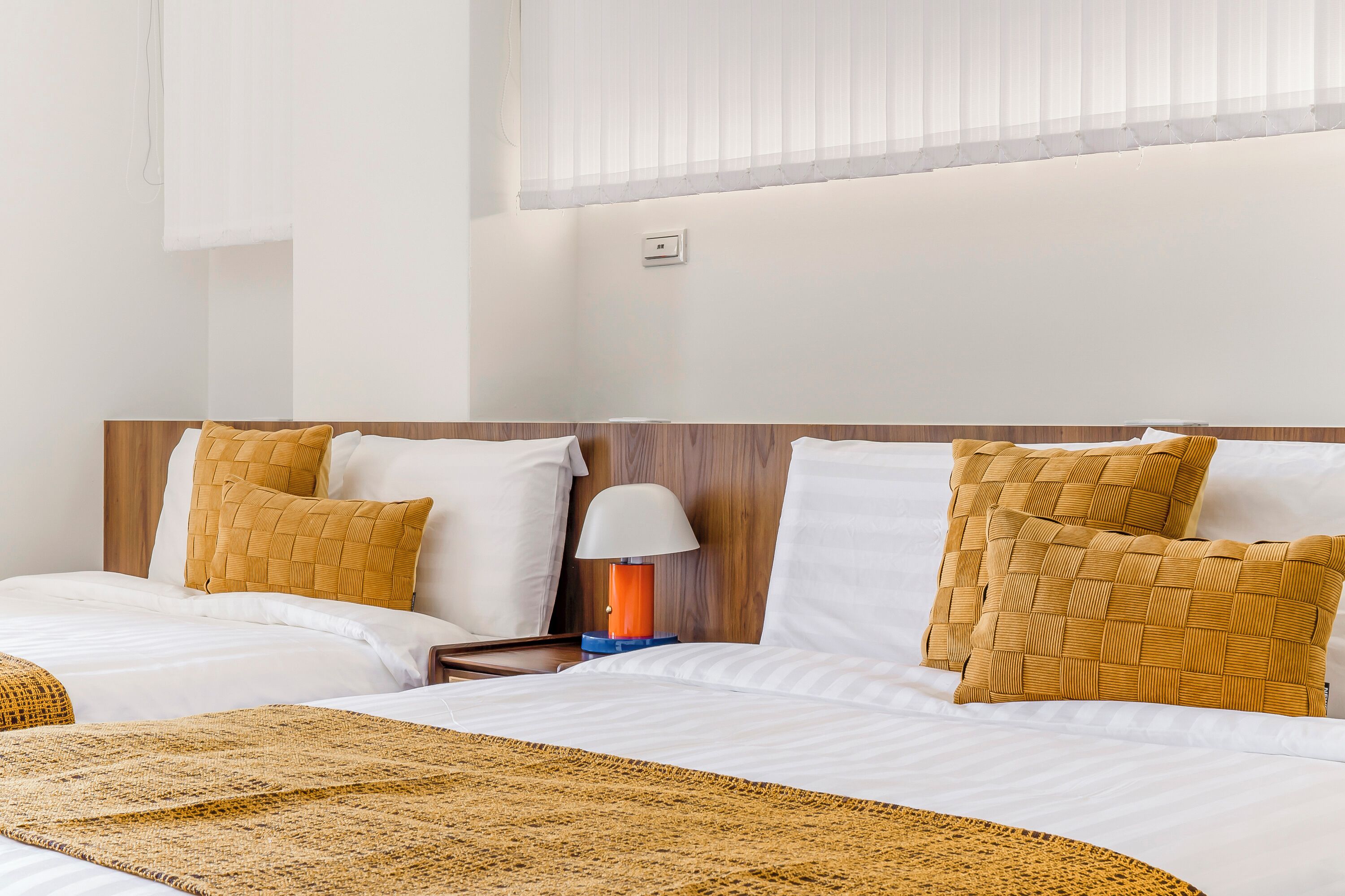 A hotel room with two beds, a wooden headboard, white bedding, and a woven throw blanket.
